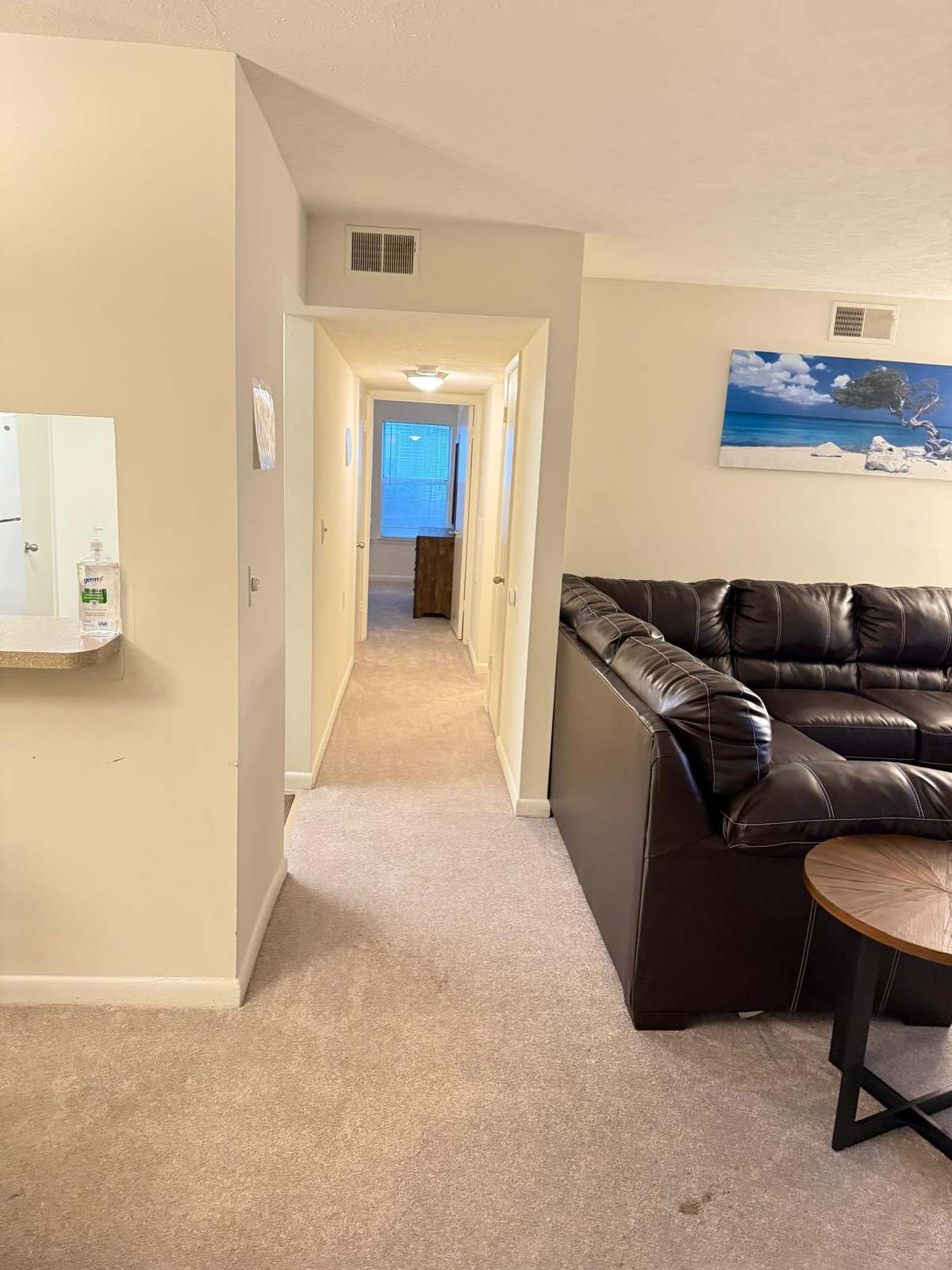 The hallway leading from the living room to the bedrooms, with a hand sanitiser dispenser mounted beside the kitchen pass-through.