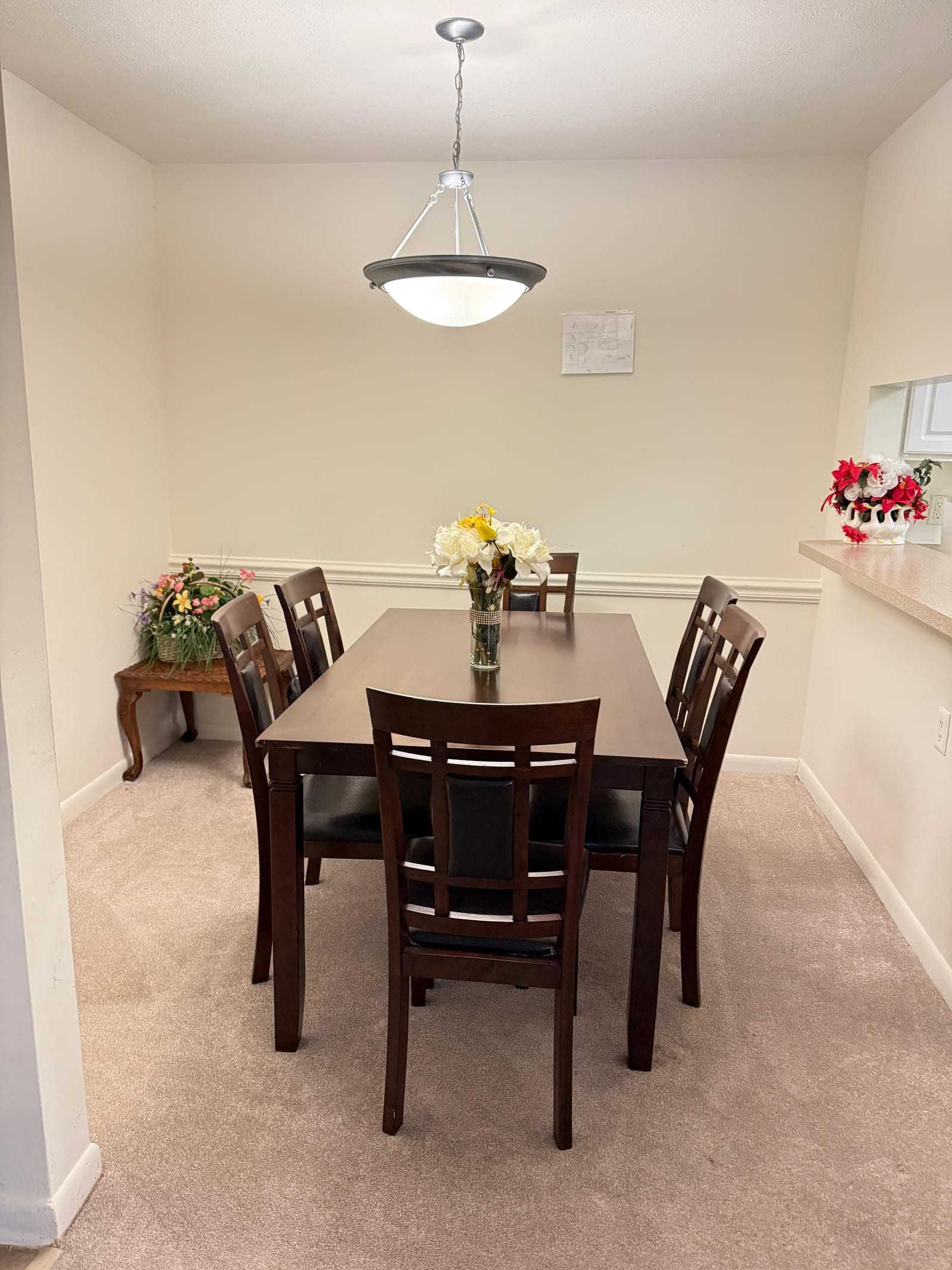 The dining room, with a wooden table set for six under a pendant light and fresh flowers in the centre.