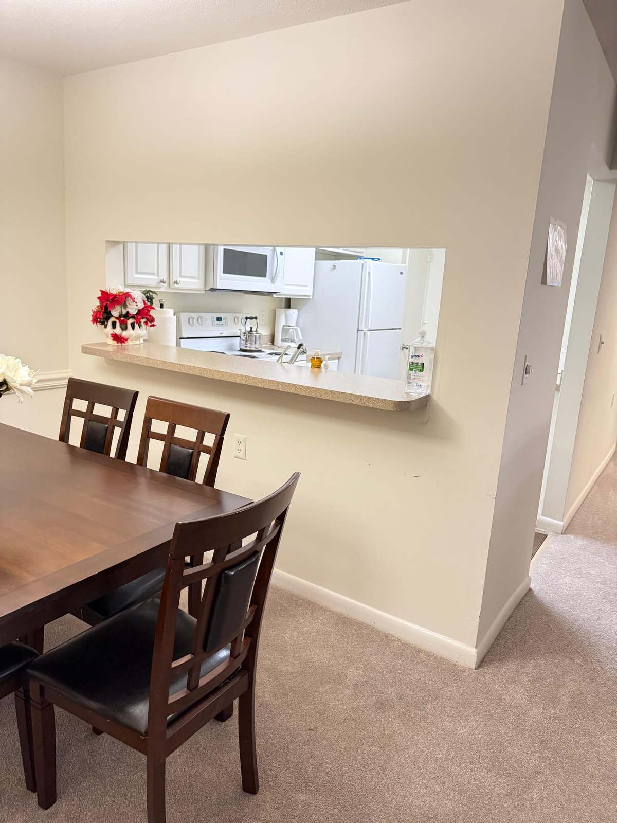 The dining table beside the open pass-through to the kitchen, looking across the counter to the cooker and refrigerator.